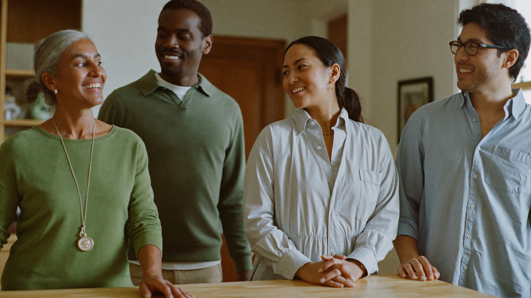 Four colleagues of different ages laughing together around a domestic kitchen island